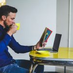 man drinking on yellow cup while reading book